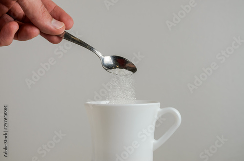 A hand spooning sugar in a white mug