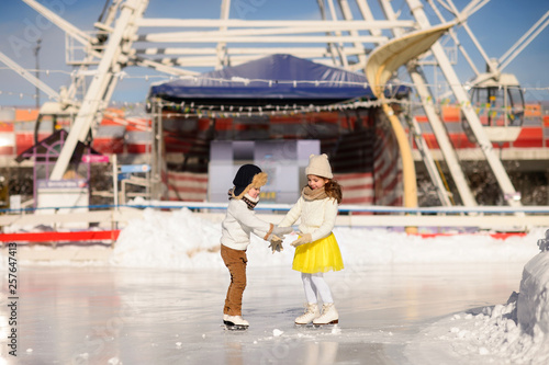 Young girl and boy ice skating at the ice rink outdoor. The girl in the yellow skirt