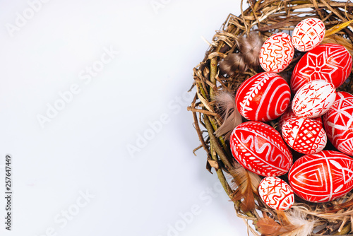 Closeup Easter red eggs with folk white pattern inside bird nest on white. Top view.