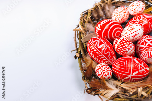 Closeup Easter red eggs with folk white pattern inside bird nest on white background. Top view.