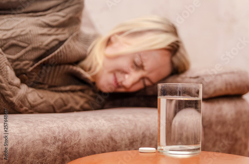 Sick girl lying on the couch, on the table are tablets