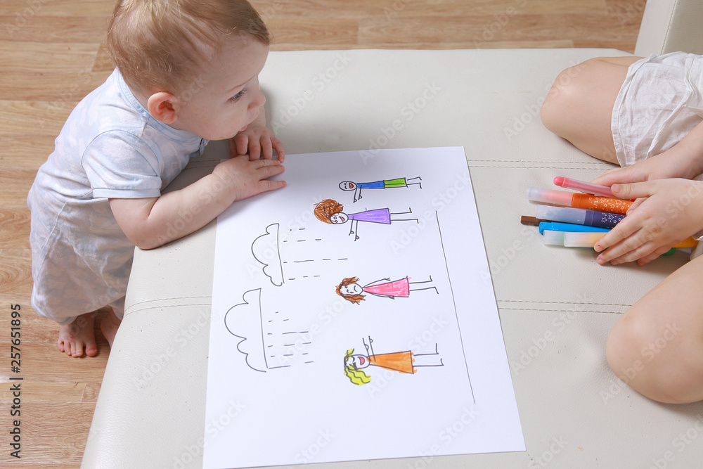 Girl draws a picture of the family. younger brother looks. Light room. condemnation, stigma Girl draws a picture of the family. younger brother looks. Light room. condemnation, stigma