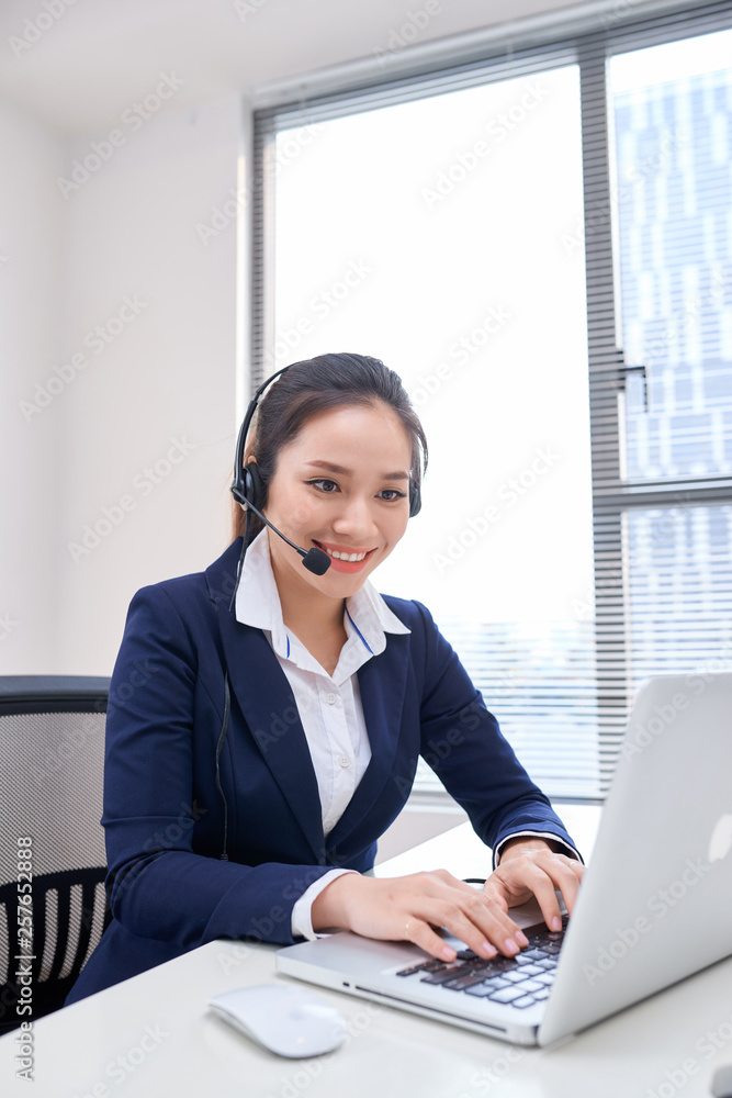 Portrait of happy smiling female customer support phone operator at workplace. Asian
