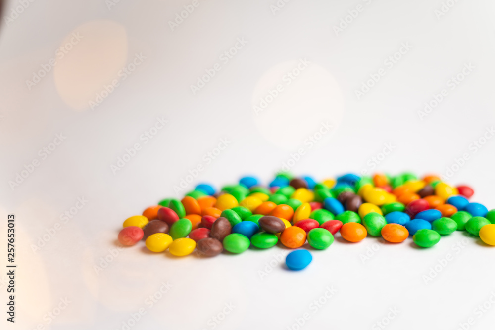 Obraz premium Coated chocolate multicolor candies on the white background with bokeh lights