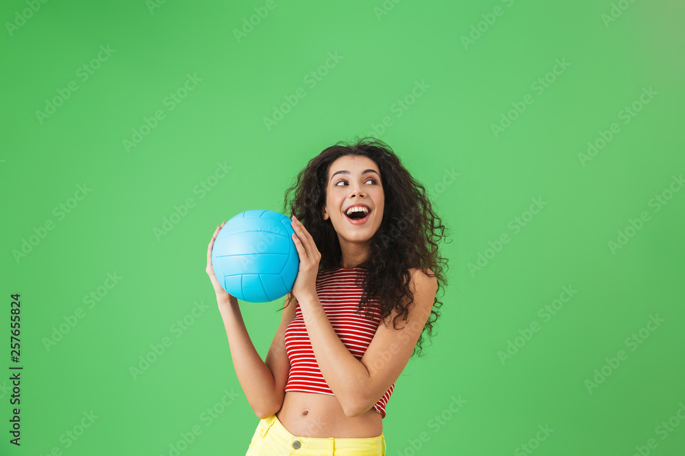 Image of happy woman 20s smiling and holding volley ball while standing against green background Image of happy woman 20s smiling and holding volley ball while standing against green background