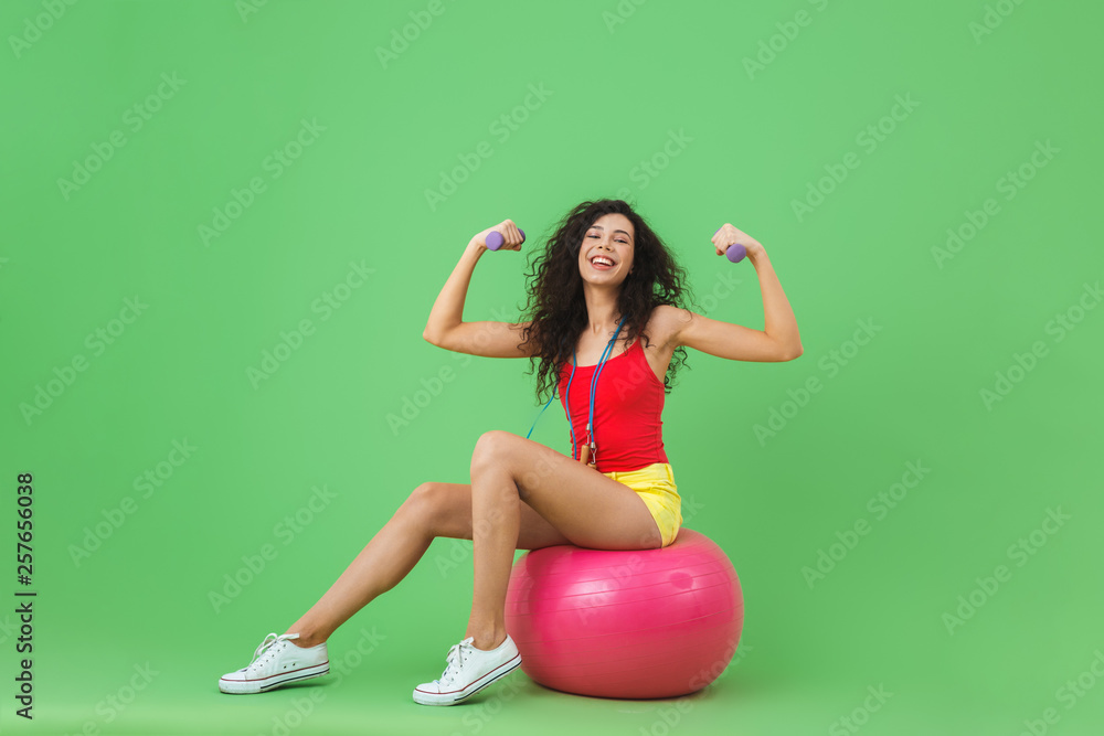 Image of brunette woman 20s wearing summer clothes lifting dumbbells while sitting on fitness ball during aerobics Image of brunette woman 20s wearing summer clothes lifting dumbbells while sitting on fitness ball during aerobics