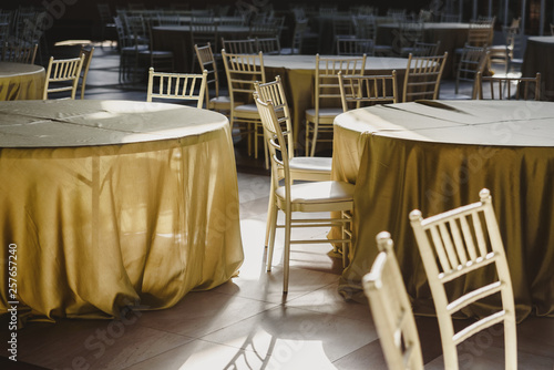 Round tables with tablecloths, empty, surrounded by wooden chairs, in a restaurant.
