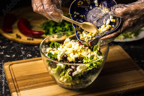 Mixing the ingredients of black bean salad, lettuce, eggs and sweet pepper in a glass bowl.