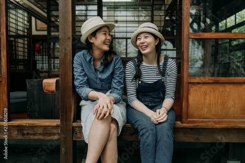 two asian women friends travel in osaka japan lifestyle moments in traditional japanese house. happy young girls in hats laughing talking chatting sitting outdoor enjoy in teien zen garden in spring. photo