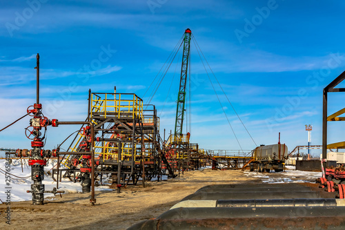Oil field in Siberia. In a row are oil producing wells. In the background  work is underway to overhaul the well. In the foreground is a manifold with valves.