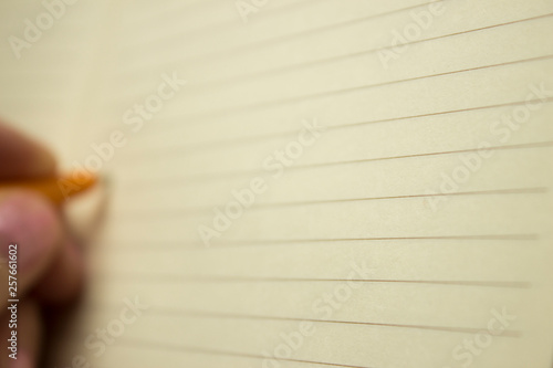 The hand of the white man writes with a ballpoint pen on a sheet of white notebook lined in a line of black stripes in the background