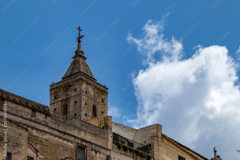 Church tower and roof with religious cross of Chiesa di Sant'Agostino, view of ancient town of Matera, Basilicata, Southern Italy, cloudy summer warm August day
