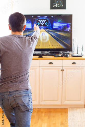 A man playing video game without joystick at home. Cheerful father with family playing bowling and having fun with new trends technology. Gaming concept
