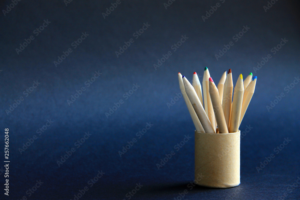 colored pencils in a round cardboard box in the right corner of the frame on a dark background concept of childhood, school, art colored pencils in a round cardboard box in the right corner of the frame on a dark background concept of childhood, school, art