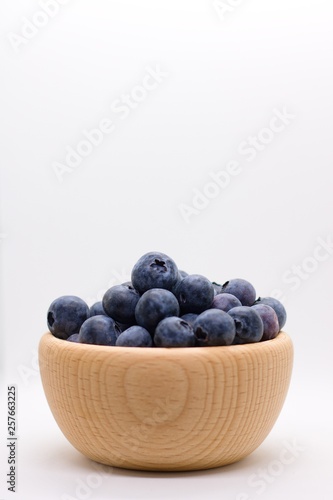 Side view of wooden bowl full of ripe juicy blueberries in wooden bowl isolated on white background with plenty of copyspace