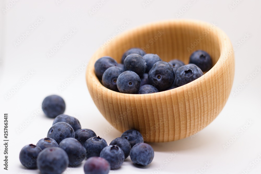 Juicy blueberries spilled out of wooden bowl isolated on white background Juicy blueberries spilled out of wooden bowl isolated on white background