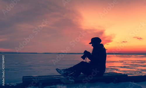 Silhouette girl photographer in the winter at sunset. A single woman takes pictures against the sky and clouds. Tourism and creativity. Copy space and picture.