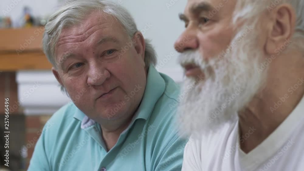 Close up of two mature senior men watching TV at home. Friends watching football soccer while eating chips. People involved in game Close up of two mature senior men watching TV at home. Friends watching football soccer while eating chips. People involved in game