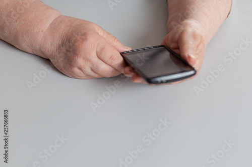  Black touchscreen phone in elderly hands on a gray background.