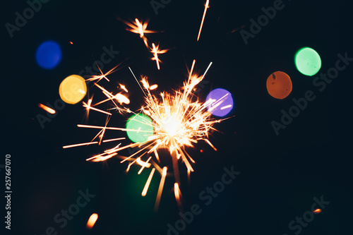 sparkling Bengal sparklers sticks in flames on a black background with lights bokeh. christmas theme new year background. holiday card