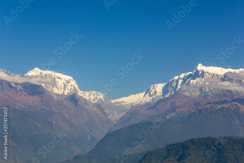 hillsides with green forests on the background of desert mountains and the snowy ridge of Annapurna under a clear blue sky. Himalayas Nepal