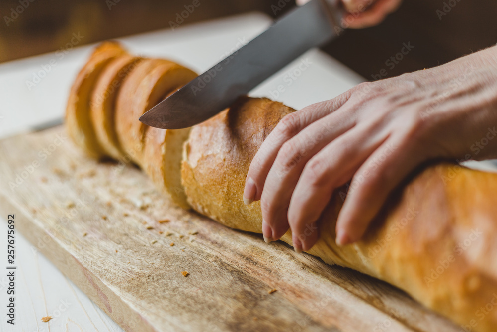 Fresh Crisp White Wheat Bread - Closeup of Female Hands Slicing Baguette Fresh Crisp White Wheat Bread - Closeup of Female Hands Slicing Baguette