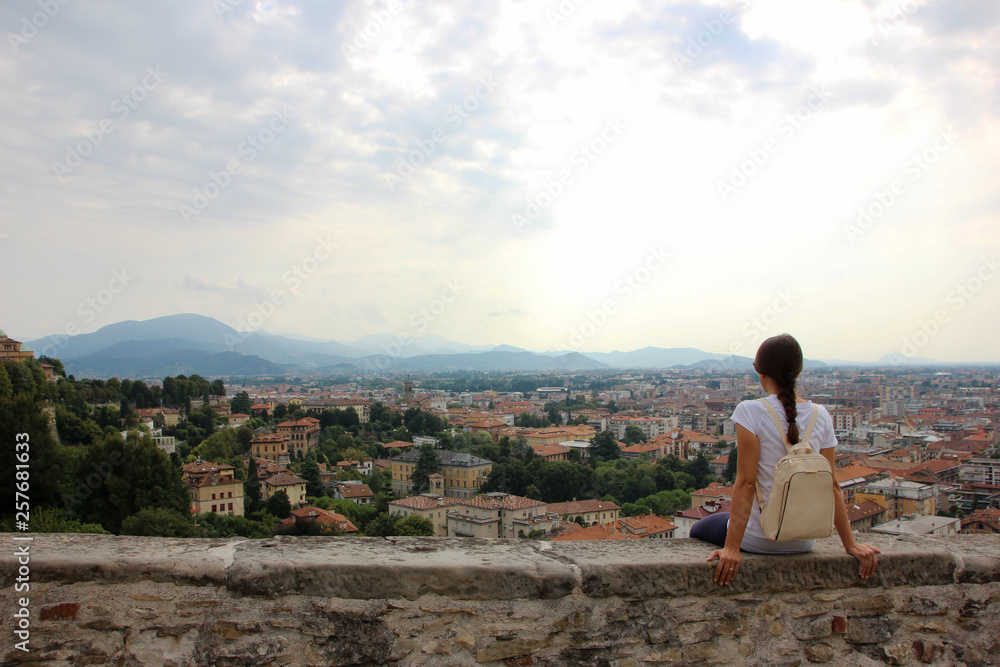 Giovane donna seduta sulle mura di Bergamo alta, porta San Giacomo. Lombardia, Italia