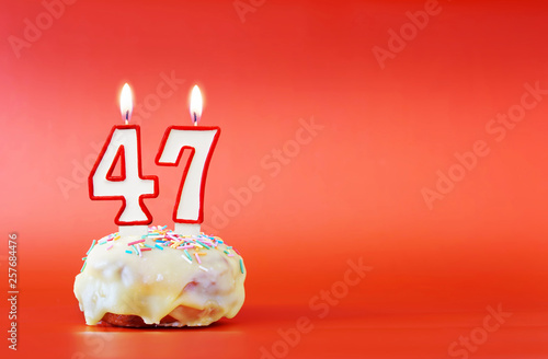 Forty seven years birthday. Cupcake with white burning candle in the form of number 47. Vivid red background with copy space