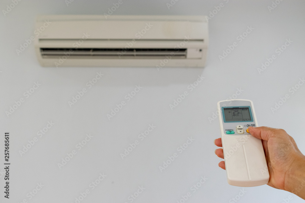 Woman's hand using remote control open The air conditioner is cooled to 25 degrees Celsius in his bedroom. Health concepts and energy savings Woman's hand using remote control open The air conditioner is cooled to 25 degrees Celsius in his bedroom. Health concepts and energy savings