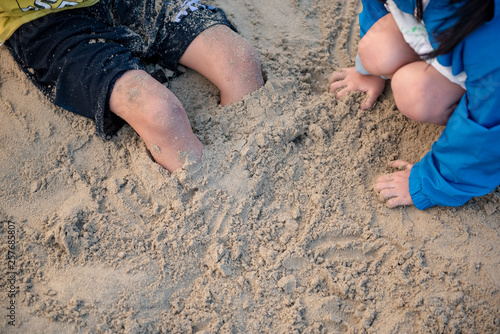 Child pours sand on his feet on sand beach in summer. photo