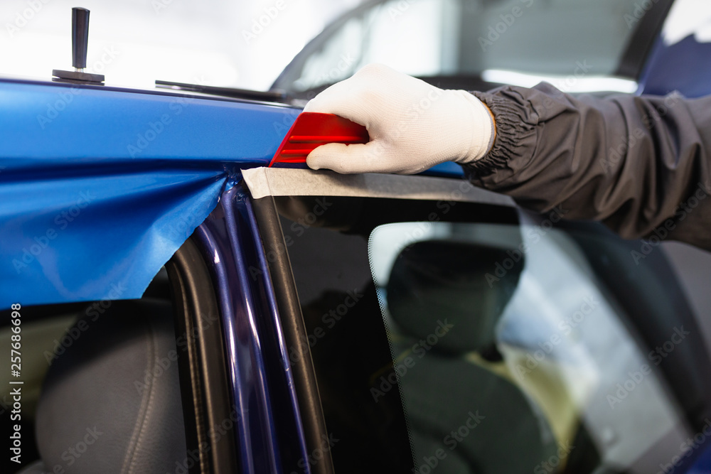 Car wrapping specialist putting vinyl foil or film on car. Selective focus.