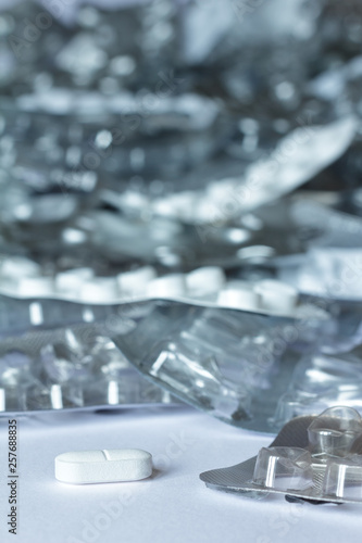 One single tablet in front of many empty blister packages on white background, drug misuse concept photo