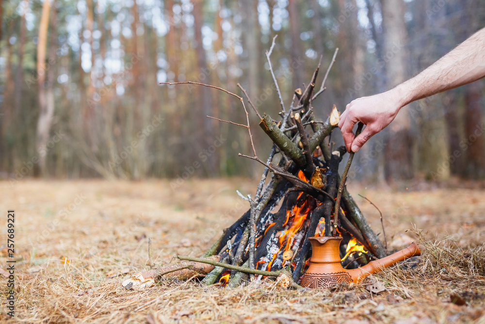 Naklejka premium At the stake in the spring forest, a clay Turkish coffee pot is heated against the grass. In the frame one man's hand.