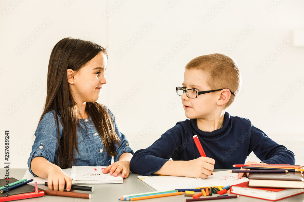 Two smiling little kids at the table draw with crayons, isolated on white Two smiling little kids at the table draw with crayons, isolated on white