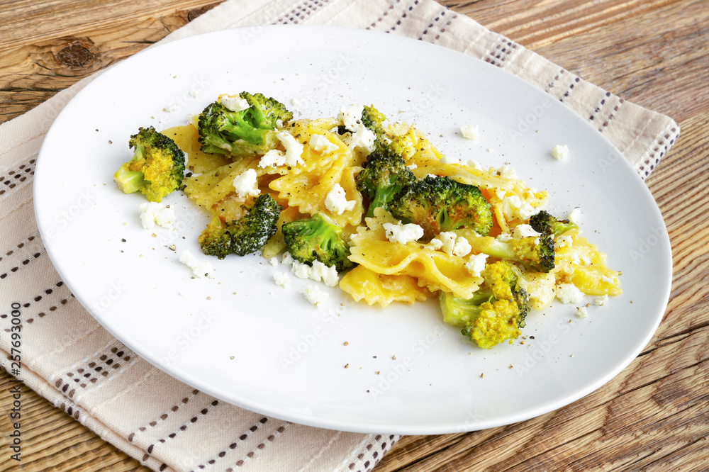 plate of boiled butterfly pasta with fried in garlic oil broccoli, feta, and black pepper on napkin. warm wooden background plate of boiled butterfly pasta with fried in garlic oil broccoli, feta, and black pepper on napkin. warm wooden background