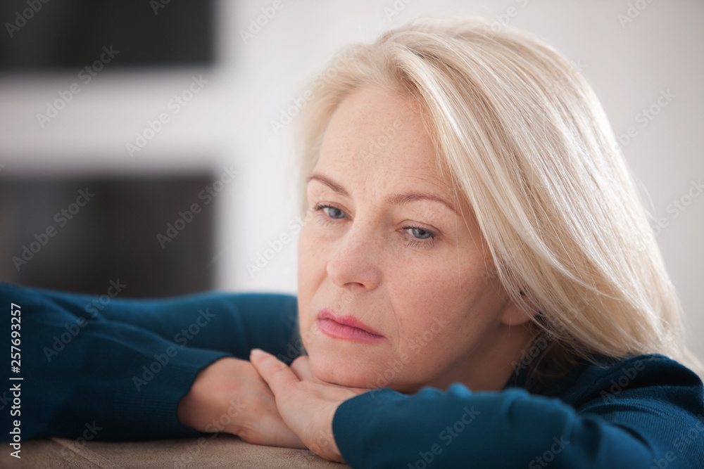 Sad woman sitting on a sofa in the living room Sad woman sitting on a sofa in the living room