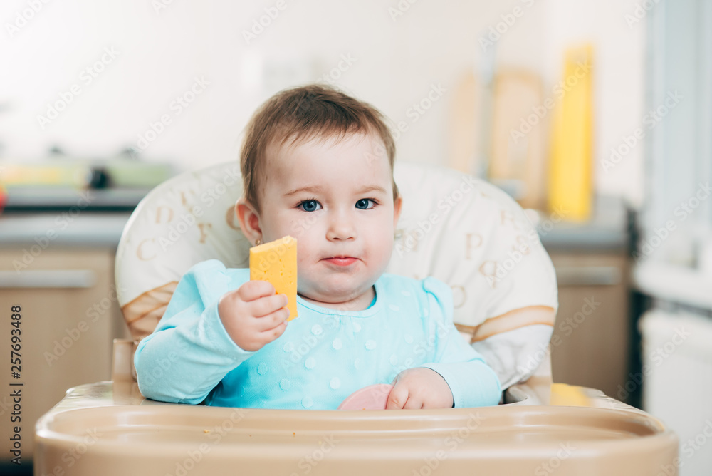 Little girl in a high chair with a piece of cheese and sausage Little girl in a high chair with a piece of cheese and sausage