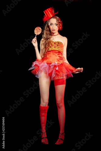 Sexy burlesque dancer stripper posing with sweet lollipop, in red corset and red hat with curly hair and beautiful legs in red stockings photo