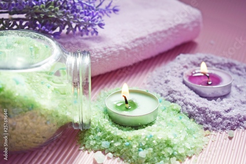 Lilac and green bath salt and candles on pink background.