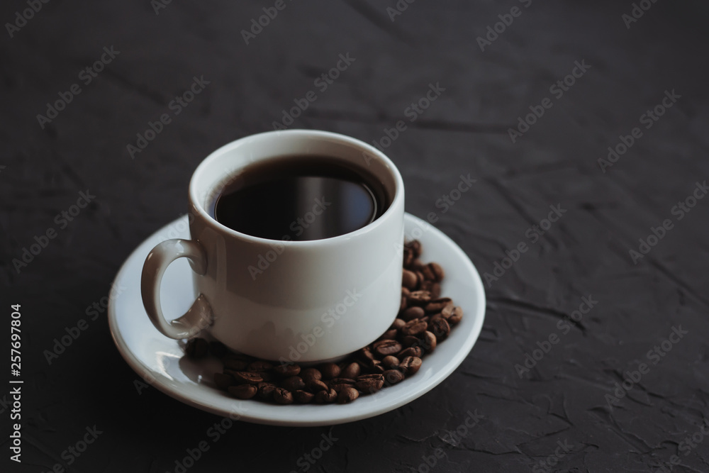 White cup of coffee and coffee beans on a dark background White cup of coffee and coffee beans on a dark background