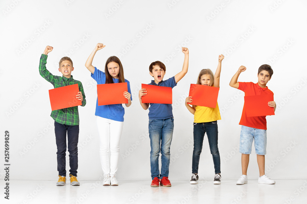 Group of screaming serious children with red empty banners isolated on white studio background. Education and advertising concept. Protest and children's rights concepts. Group of screaming serious children with red empty banners isolated on white studio background. Education and advertising concept. Protest and children's rights concepts.