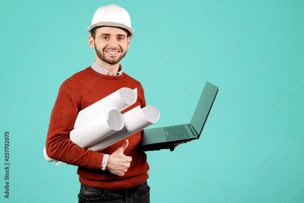 Attractive young handsome bearded engineer or constructor man in casual outfit holding notebook or computer over cyan background. Architecture and Renovation concept. Attractive young handsome bearded engineer or constructor man in casual outfit holding notebook or computer over cyan background. Architecture and Renovation concept.