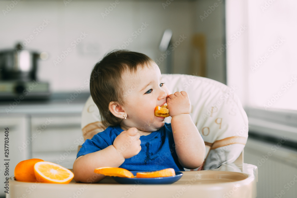 little girl sitting in baby chair, eating an orange little girl sitting in baby chair, eating an orange