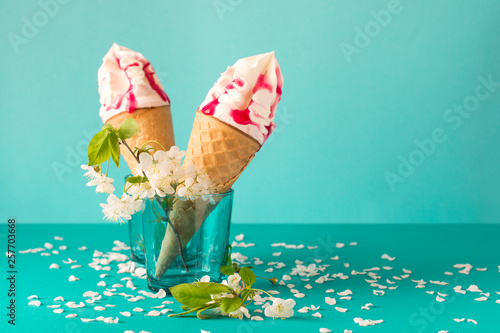 Melting ice cream cone with fruit syrup decorated white cherry blossom on blue background
