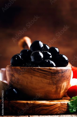 Принти на полотні Spanish black olives in olive wooden bowl, rustic kitchen table background, sele