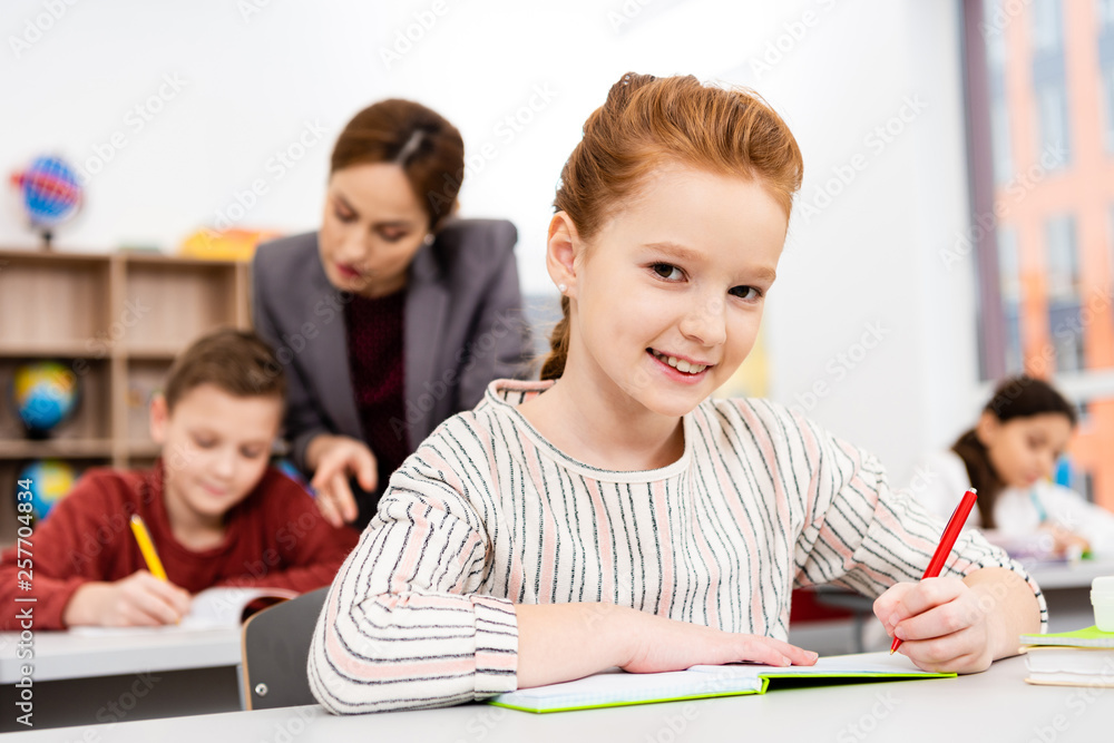 Cute ginger schoolgirl writing in notebook during lesson in classroom Cute ginger schoolgirl writing in notebook during lesson in classroom