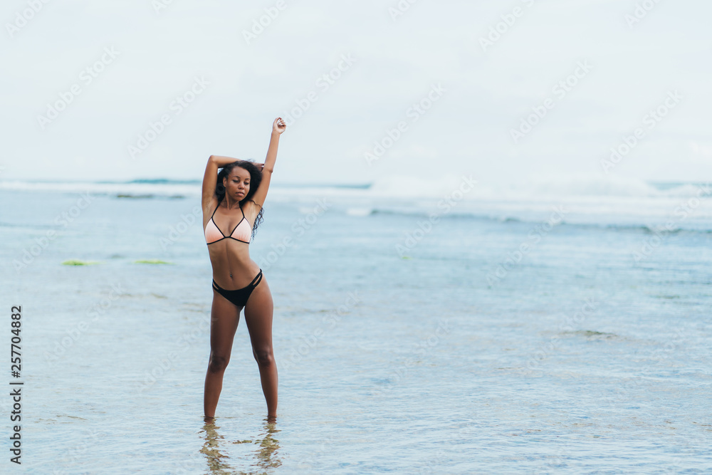 Beautiful dark skinned girl in swimwear resting on beach. African american model posing on tropical island Beautiful dark skinned girl in swimwear resting on beach. African american model posing on tropical island