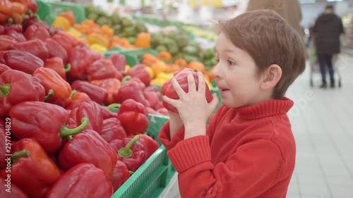 little boy in supermarket smelling red bulgarian peppers. Shopping in store, fresh products for kitchen and cooking.