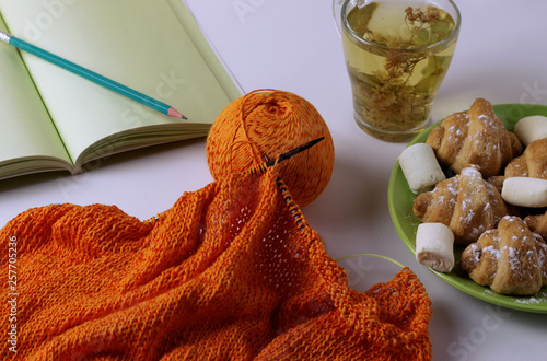 On the table lies a knitting of orange yarn, next to it is lime tea and delicious croissants with mashmelow. Home furnishings for rest. Blur effect photo