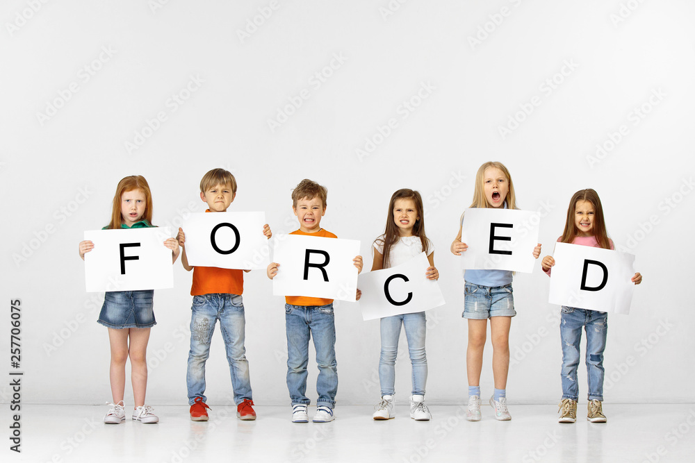 Obraz premium Being forced is prison. Group of angry screaming children with a white banners holding word isolated in studio background. Education, advertising and social rights concept.